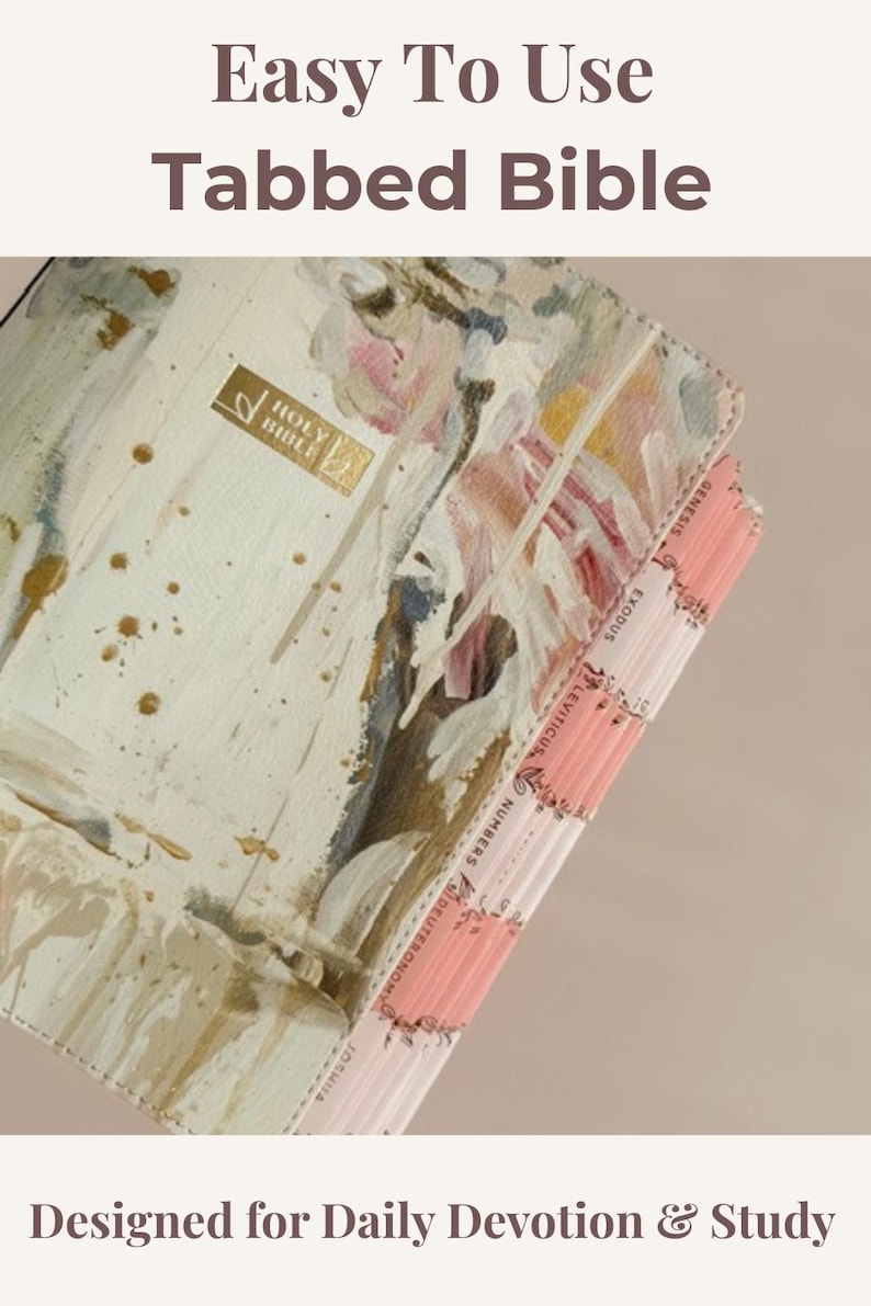 May include: A Bible with a cream-colored cover featuring an abstract painted design in shades of pink, green, and gold. The cover includes a gold-stamped Holy Bible emblem. The side features pink index tabs labeled Genesis, Exodus, Leviticus, Numbers, Deuteronomy, and Joshua.
