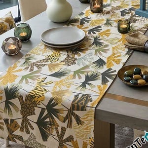 Puede incluir: Una mesa de comedor con un camino de mesa estampado con diseños de hojas y animales en amarillo, verde y marrón. La mesa está puesta con platos, velas y objetos decorativos, creando un ambiente acogedor.