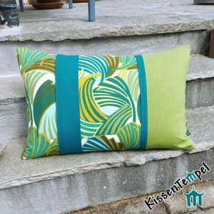 Può includere: Un cuscino con motivo verde, turchese e bianco con un pannello in tessuto verde tinta unita sul lato destro. Il cuscino è su un set di gradini in cemento.