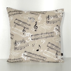 Peut inclure: Coussin carré beige avec un motif répété de notes de musique, de clés de sol et de volutes décoratives en noir et blanc. Le coussin est fait d'un tissu texturé, idéal pour la décoration intérieure.
