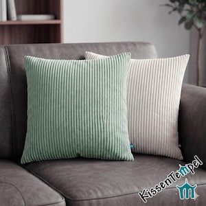 Könnte beinhalten: Zwei Kissen aus Cord in Salbeigrün und Creme liegen auf einem dunkelgrauen Sofa. Die Kissen haben eine vertikale Rippenstruktur. Die quadratischen Kissen verleihen dem Wohnzimmer Textur und Farbe.