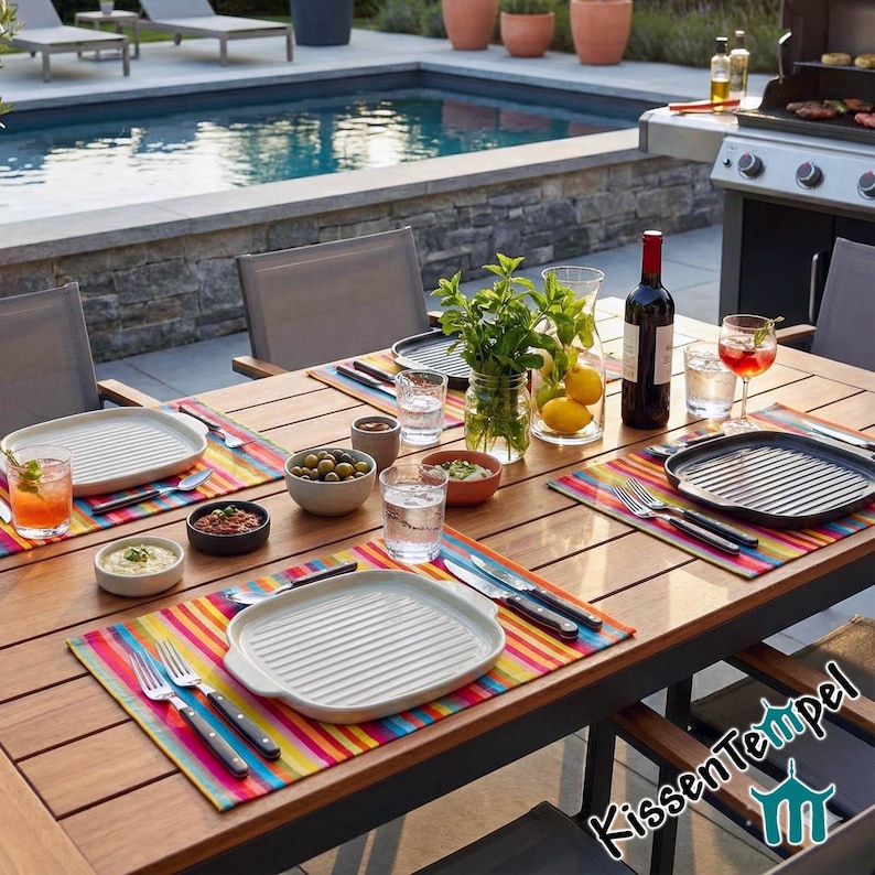 Puede incluir: Una mesa de comedor de madera al aire libre, con platos blancos, manteles individuales a rayas de colores y varios alimentos. Una piscina y una parrilla son visibles en el fondo, lo que sugiere un entorno de jard&iacute;n.