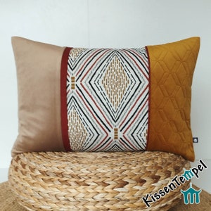 Op de afbeelding: Een rechthoekig kussen met een geometrisch patroon in tinten bruin, rood en wit. Het kussen is gemaakt van een zachte, textuurrijke stof en heeft een gestikte achterkant.