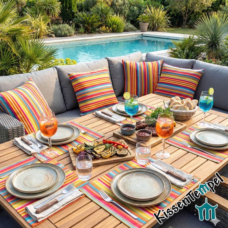 Puede incluir: Escena de comedor al aire libre con una mesa de madera, asientos acolchados grises y coloridos cojines a rayas. La mesa est&aacute; puesta con platos, cubiertos y vasos. Se sirven verduras a la parrilla y pan, junto con bebidas. Una piscina es visible en el fondo.