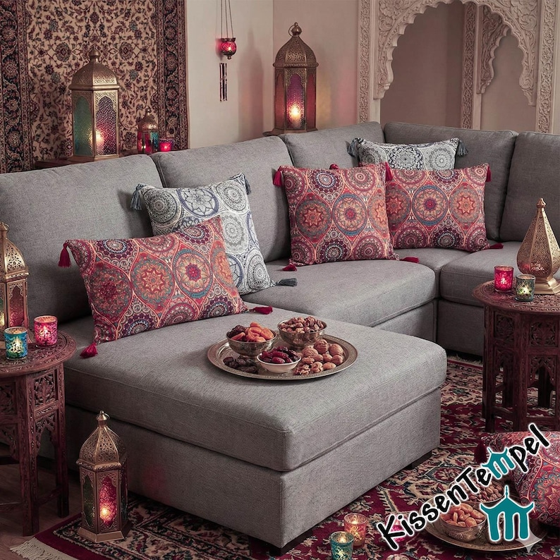 May include: A gray sectional sofa with patterned throw pillows in shades of red, blue, and white. Decorative lanterns and small tables with candles and a tray of snacks create a cozy, inviting living space. The scene evokes a warm, Middle Eastern aesthetic.