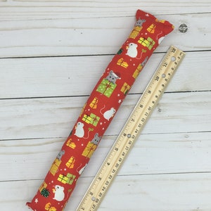 May include: A red and white cat toy shaped like a long, thin tube with a Christmas theme. The toy is covered in a fabric with a pattern of small white mice and green and yellow gift boxes. The toy is 12 inches long.