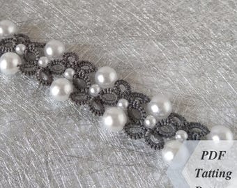 Pode incluir: Um bracelete de renda de tatting cinza com pérolas brancas. O bracelete está sobre um fundo prateado. O texto "PDF Tatting Pattern" está no canto inferior direito da imagem.