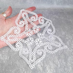 Könnte beinhalten: Weiße gehäkelte Spitzendeckchen mit quadratischer Form und einem zarten Blumenmuster.
