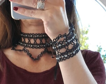 Pode incluir: Um conjunto de colar e pulseira preto com contas prateadas. O colar é em camadas e a pulseira é feita de várias camadas.