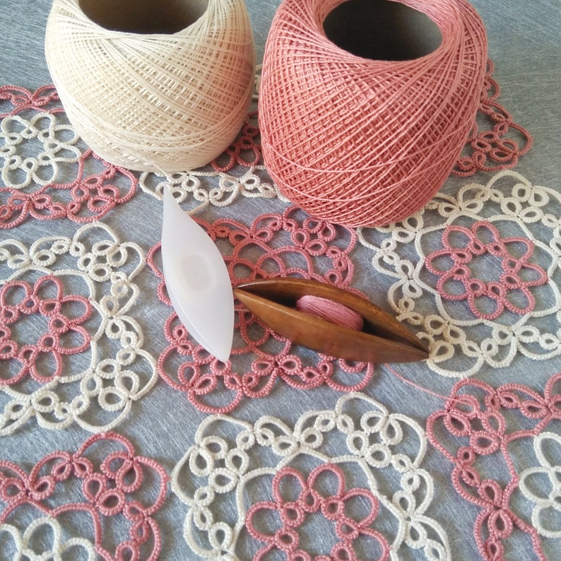 Pink and ecru table napkin with shuttles and thread on top of it