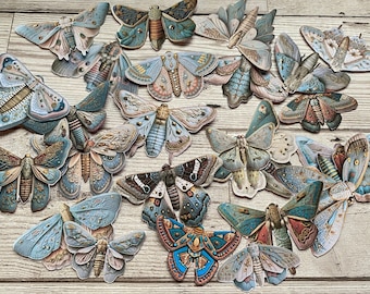 Può includere: Una collezione di 15 farfalle di carta con disegni intricati in tonalità di blu, verde e oro. Le farfalle hanno un'estetica vintage e sono perfette per l'artigianato o la decorazione.