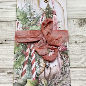 May include: A set of three Christmas-themed bookmarks with a red ribbon and a red tassel. The bookmarks feature a watercolour design of holly, candy canes, and a deer.