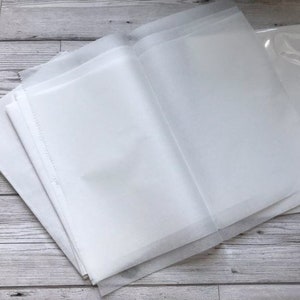 Pu&ograve; includere: Un mucchio di fogli di carta velina bianca, piegati a met&agrave;, con un foglio di plastica trasparente sopra.