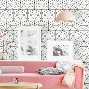 Puede incluir: Salón moderno con sofá de terciopelo rosa, mesa de centro redonda de madera y papel pintado geométrico. Cojines decorativos y una manta rosa añaden color. Dos impresiones en blanco y negro enmarcadas cuelgan sobre el sofá.