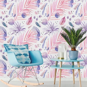 May include: A light blue rocking chair with a blue and white tie-dye cushion sits in front of a wall with a pink and purple watercolor tropical leaf pattern. A light blue side table with a wooden base sits next to the chair. A potted green plant sits on the table.