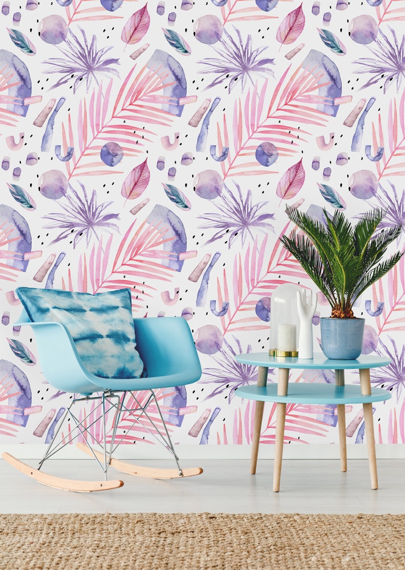 May include: A light blue rocking chair with a blue and white tie-dye cushion sits in front of a wall with a pink and purple watercolor tropical leaf pattern. A light blue side table with a wooden base sits next to the chair. A potted green plant sits on the table.