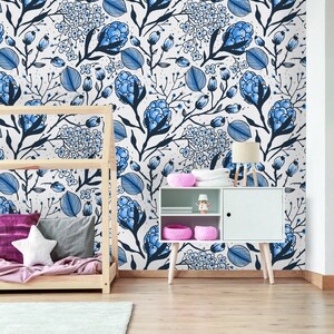 Puede incluir: Una pared blanca con un patr&oacute;n de papel tapiz floral azul y blanco. Un marco de cama de madera con una manta rosa y morada est&aacute; en primer plano. Un gabinete blanco con un estante y una cesta rosa est&aacute; en primer plano. Una l&aacute;mpara est&aacute; en el gabinete.