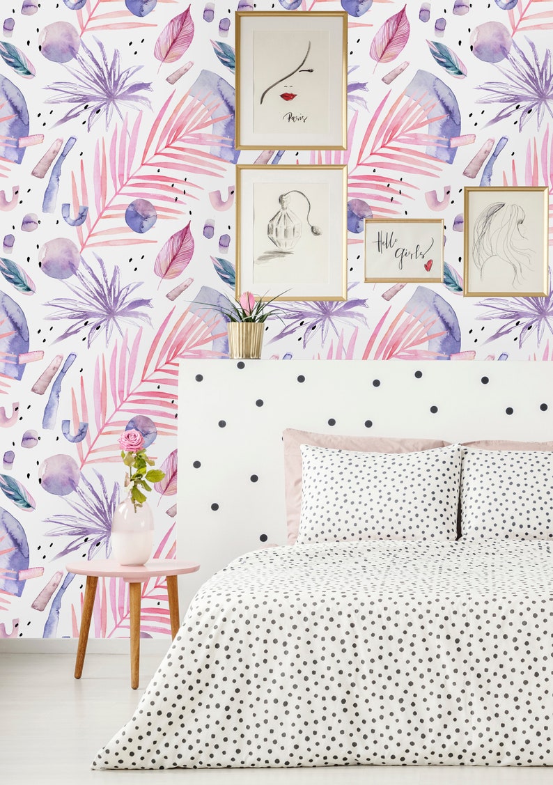 May include: A white bed with a black polka dot duvet cover and matching pillowcases. The headboard is white with black polka dots. The wall behind the bed is covered in a pink and purple floral wallpaper with abstract shapes. There are three framed pictures on the wall, one with the word "Paris" on it, one with a drawing of a perfume bottle, and one with the text "Hello girls!"