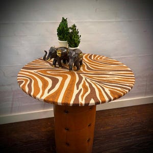 May include: A round side table with a zebra print top and a brown leather-like base. Two small bronze elephant figurines and two potted green plants sit on top. The table is approximately 24 inches in diameter.