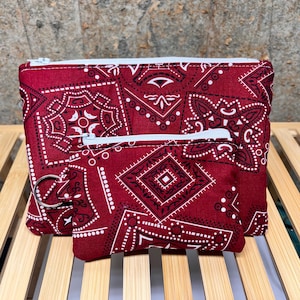 May include: A set of two rectangular pouches made of dark red fabric with a white geometric bandana-style print. Both pouches feature a white zipper closure at the top. The smaller front pouch includes a silver metal split ring attached to the side.