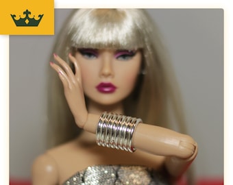 May include: A doll with blonde hair wearing a silver bangle bracelet. The bracelet is made of multiple stacked rings.