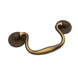 May include: A brass cabinet pull with a curved handle and round knobs. The pull has a brushed finish.