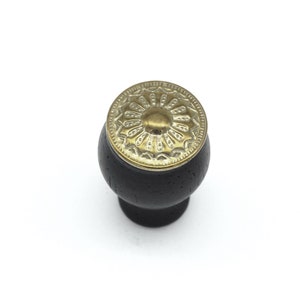 May include: Black wooden cabinet knob with a gold metal decorative top featuring a floral design.