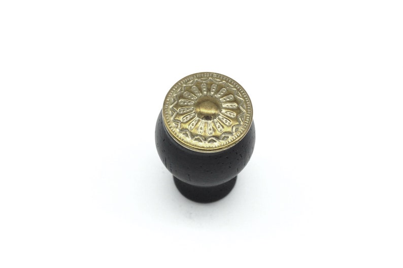 May include: Black wooden cabinet knob with a gold metal decorative top featuring a floral design.