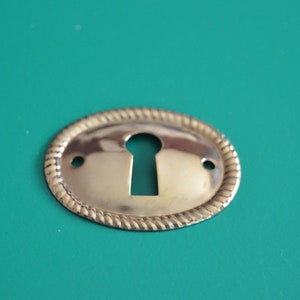 May include: A gold-colored oval keyhole cover with a rope-like design around the edge.