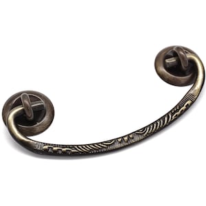 May include: A decorative antique-style cabinet pull with a curved design and ornate details. The pull is made of metal and has a dark bronze finish.
