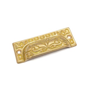 May include: Gold-toned metal drawer pull with a decorative floral design. The pull has a rectangular shape with rounded edges and a recessed center.