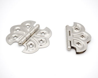 May include: Two silver butterfly-shaped hinges with a decorative design. The hinges are closed and have a polished finish.