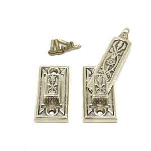 May include: Two antique brass door latches with ornate floral and geometric designs. The set includes two rectangular base plates, a pivoting latch, and several small brass screws. The hardware is set against a white background.