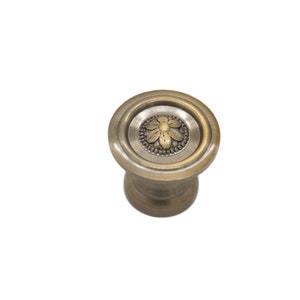 May include: A round, antique gold cabinet knob with a decorative floral design in the center.