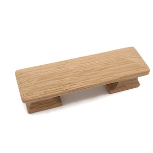 May include: A rectangular wooden cabinet pull with a light brown finish. The pull has a flat top and two decorative supports. The wood grain is visible. This hardware is suitable for drawers and cabinets.