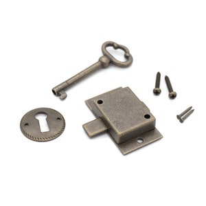 May include: Antique bronze-toned cabinet hardware set, including a key, keyhole cover, latch, and screws. The key has a decorative handle. The keyhole cover has a textured edge. The latch is rectangular. Ideal for vintage furniture restoration.