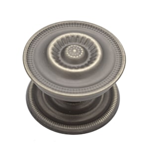 May include: A silver-toned door knob with a decorative, raised, circular design. The knob has a round base and a raised, circular top.