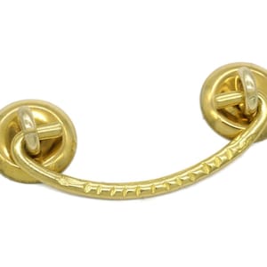 May include: A gold-toned drawer pull with a curved handle and two circular backplates. The handle has a textured, ridged design. Hardware for cabinets, drawers, or furniture.