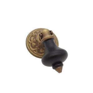 May include: A black wooden knob with a brass base and ornate design. The knob is shaped like a bell and has a pointed tip.