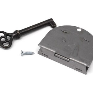 May include: A silver-toned metal lock with a keyhole and a small screw. The lock has a curved shape and a keyhole on the top. The key is made of dark metal and has a decorative design.