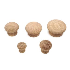 May include: Five wooden cabinet knobs in varying sizes. The knobs are made of light-colored wood with a natural grain pattern. The knobs are round with a flat base and a rounded top, suitable for furniture hardware.