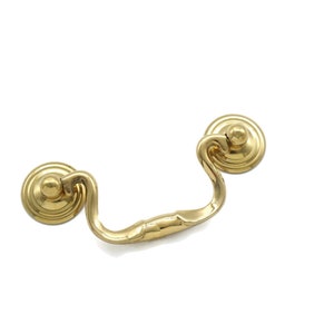 May include: A gold-toned metal cabinet pull with a curved handle and two round knobs.