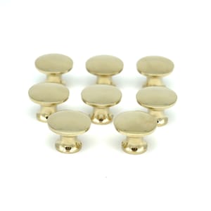 May include: Eight brass cabinet knobs with a round top and a short, cylindrical base.