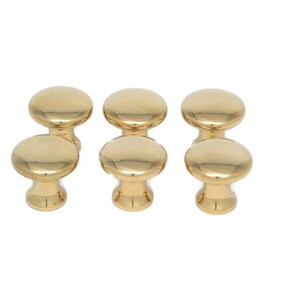 May include: Six gold-colored cabinet knobs with a smooth, rounded design. The knobs are arranged in two rows of three, showcasing their polished, reflective surface. These knobs are suitable for furniture and cabinet hardware.