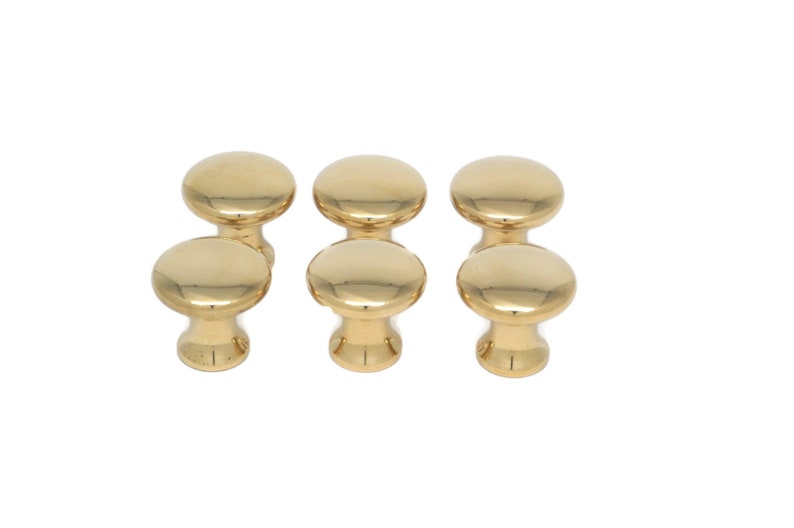 May include: Six gold-colored cabinet knobs with a smooth, rounded design. The knobs are arranged in two rows of three, showcasing their polished, reflective surface. These knobs are suitable for furniture and cabinet hardware.