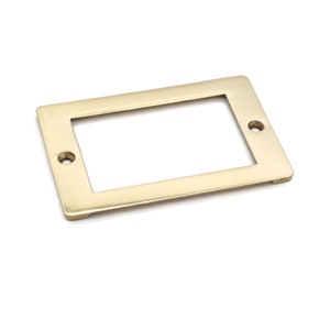 May include: A rectangular brass label holder with a recessed center and two screw holes. The label holder has a polished finish and is designed for use on drawers, cabinets, or other furniture. The hardware is a warm gold color.