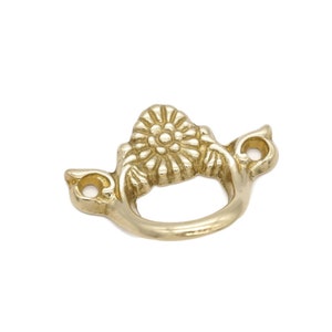 May include: A gold-toned metal drawer pull with a decorative floral design. The pull has a ring shape and two small side loops.