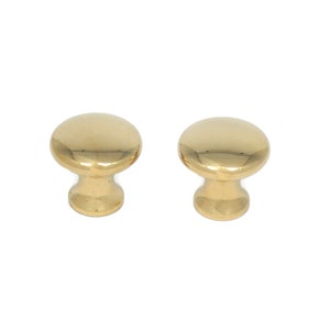 May include: Two polished brass cabinet knobs. Each knob has a rounded top and a short, cylindrical base. The knobs are a bright, shiny gold color and are set against a white background. These knobs are suitable for furniture and cabinet hardware.