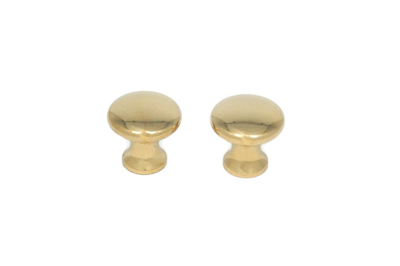 May include: Two polished brass cabinet knobs. Each knob has a rounded top and a short, cylindrical base. The knobs are a bright, shiny gold color and are set against a white background. These knobs are suitable for furniture and cabinet hardware.