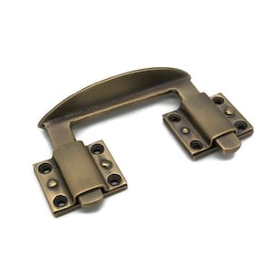 May include: Antique brass-toned cabinet handle with a curved top and rectangular mounting plates. The handle has a U-shape design with visible screw holes for installation. A classic hardware piece.
